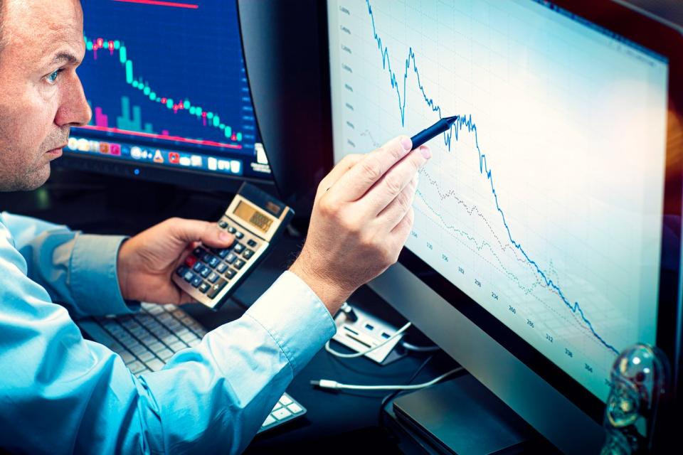 A wealth manager uses a stylus and a calculator to analyze a stock chart on a computer screen.