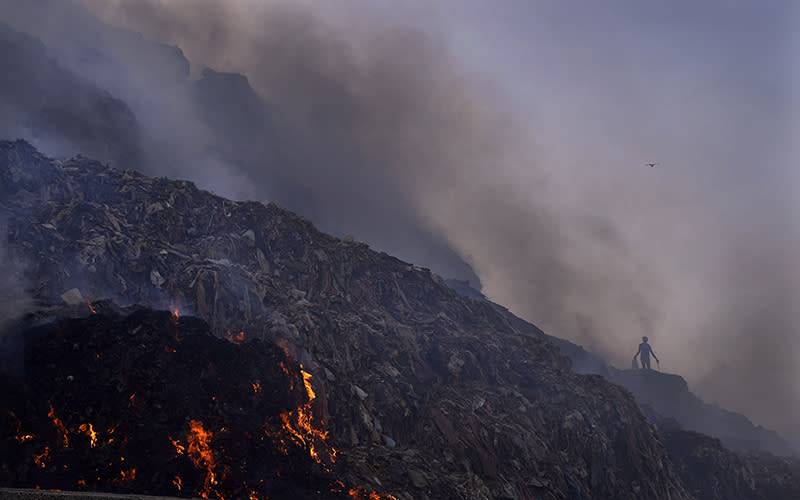 A ragpicker looks for reusable items while a fire rages at the Bhalswa landfill in New Delhi, India, on April 27. The landfill that covers an area bigger than 50 football fields, with a pile taller than a 17-story building, caught fire Tuesday evening, turning into a smoldering heap that blazed well into the night. India’s capital, which like the rest of South Asia is in the midst of a record-shattering heat wave, was left enveloped in thick acrid smoke. <em>Associated Press/Manish Swarup</em>