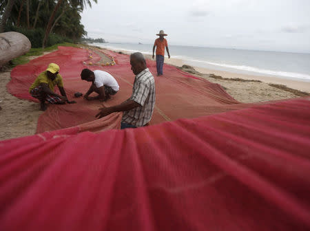 Fishermen stitch their fishing net on the beach in Seenigama December 20, 2014. REUTERS/Dinuka Liyanawatte