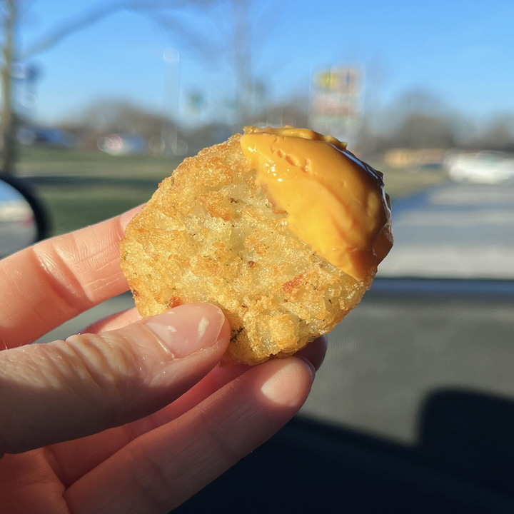 A close-up of my hand holding a mini hash brown dipped in spicy queso cheese.