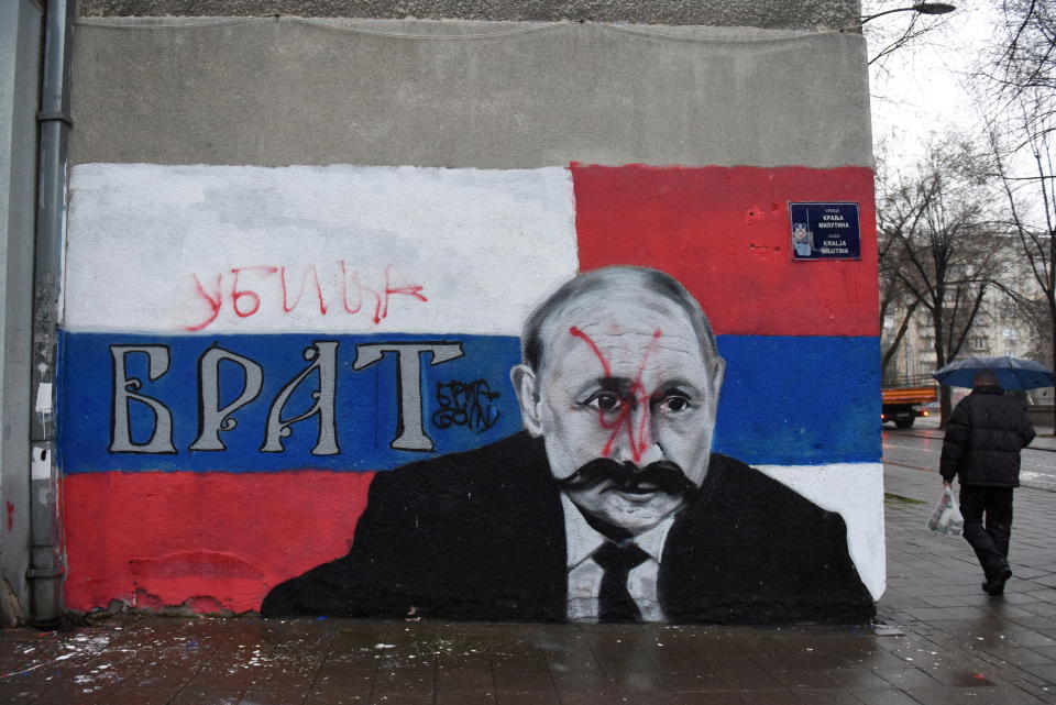 Un hombre camina junto a un mural del presidente ruso Vladimir Putin, que ha sido destrozado con pintura en aerosol roja y la palabra 