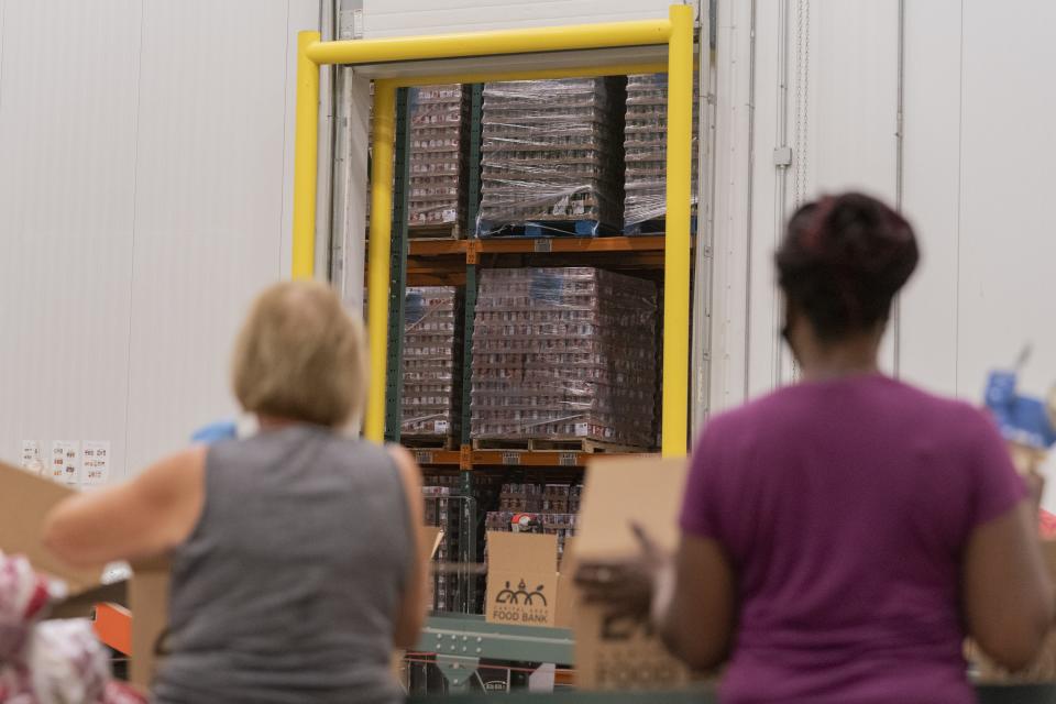 With the warehouse of food items seen through the warehouse door, volunteers pack boxes of food at The Capital Area Food Bank, Tuesday, Oct. 5, 2021, in Washington. (AP Photo/Jacquelyn Martin)