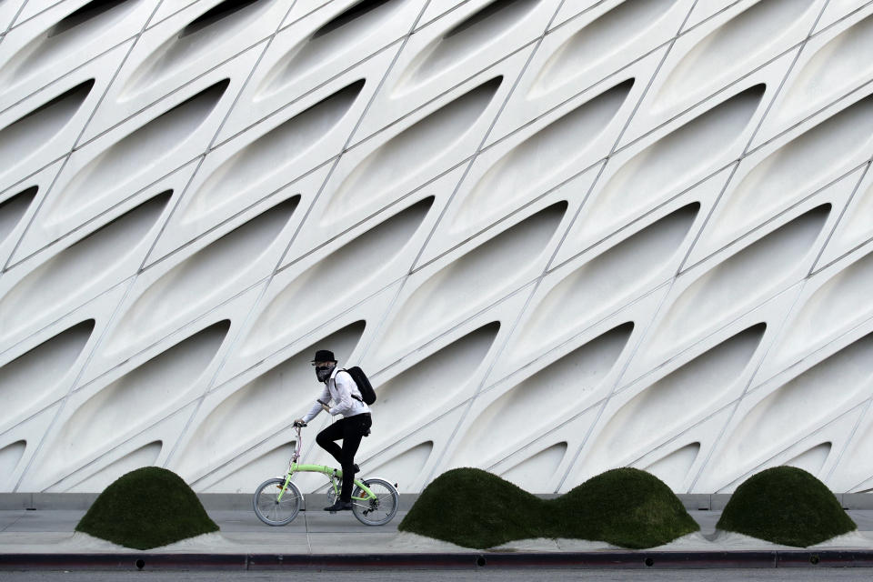 William Iwneferi wears a mask as he rides past The Broad Museum on Wednesday, April 1, 2020, in Los Angeles. Los Angeles Mayor Eric Garcetti has recommended that the city's 4 million people wear masks when going outside amid the spreading coronavirus. (AP Photo/Marcio Jose Sanchez)