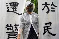 A woman wears a raincoat stands next to banners that read "The duty fulfilled by the police belongs to the people" as people take part in a rally to support the Hong Kong's Police at Edinburgh Place in Hong Kong, Sunday, Aug. 25, 2019. (AP Photo/Vincent Yu)