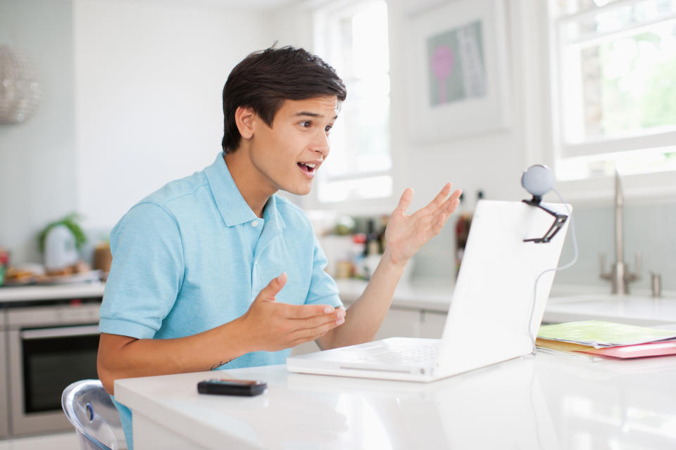 Young male adult at laptop, gesturing as if on a videoconference