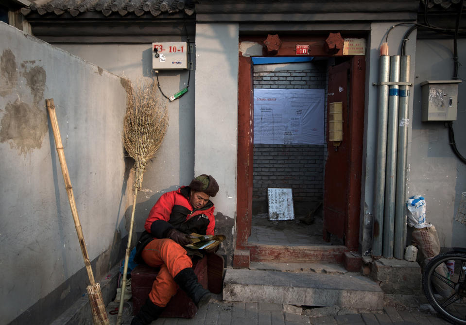 In this photo taken on Dec. 26, 2012, a street worker takes a rest near an entrance door of a Hutong home with a demolition notice on its wall near the historical Drum and Bell Tower in Beijing. The district government wants to demolish these dwellings, move their occupants to bigger apartments farther from the city center and redevelop a square in 18th century Qing Dynasty fashion. (AP Photo/Andy Wong)
