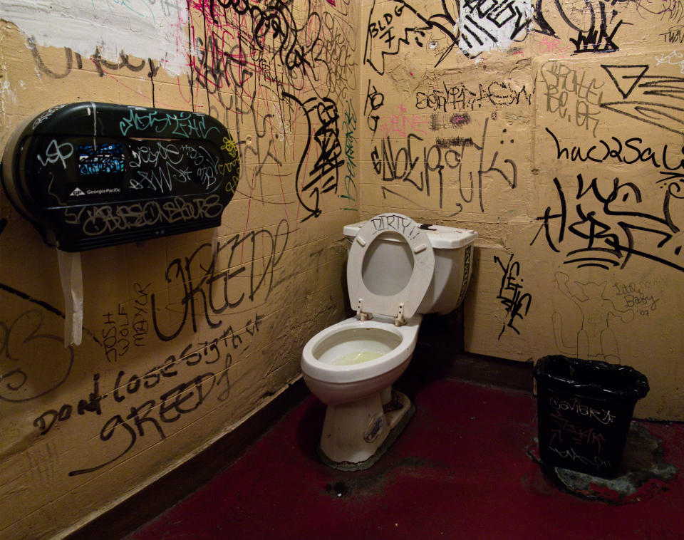 A graffiti-covered bathroom with a messy toilet and graffiti on the walls