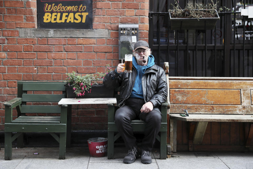 David Legge enjoys a pint and a pipe outside Bittles Bar in Belfast, Northern Ireland, Wednesday, Oct. 14, 2020. Northern Ireland introducing the tightest COVID-19 restrictions in the United Kingdom on Wednesday, closing schools for two weeks and pubs and restaurants for a month. “This is not the time for trite political points," First Minister Arlene Foster told lawmakers at the regional assembly in Belfast. “This is the time for solutions." (Brian Lawless/PA via AP)