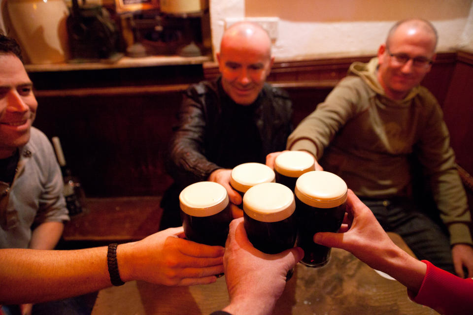 Group of men in pub raising glasses of stout in celebration.