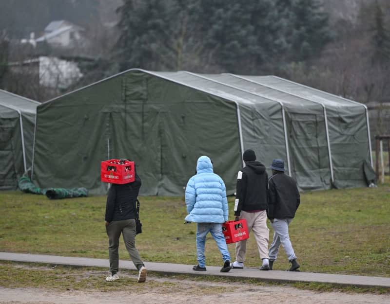 Migrants carry crates of beer to their accommodation on the grounds of the Brandenburg Central Reception Center for Asylum Seekers (ZABH) in Eisenhuettenstadt. Ministers from the member states of the European Union will meet in Brussels on Tuesday to finalize a massive overhaul of the bloc's migration and asylum laws. Patrick Pleul/dpa