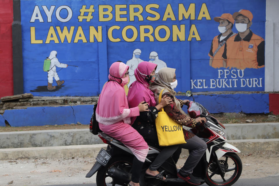 Muslim women ride a motorbike past a coronavirus-themed mural in Jakarta, Indonesia, Thursday, Sept. 10, 2020. Writings on the mural read "Let's fight coronavirus together". As companies race to develop a COVID-19 vaccine and countries scramble to secure doses, questions about the use of pork products — banned by some religious groups — has raised concerns about the possibility of disrupted immunization campaigns. (AP Photo/Tatan Syuflana)