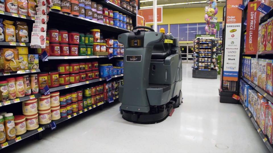 A riding floor scrubber without a driver navigating an aisle at Walmart.