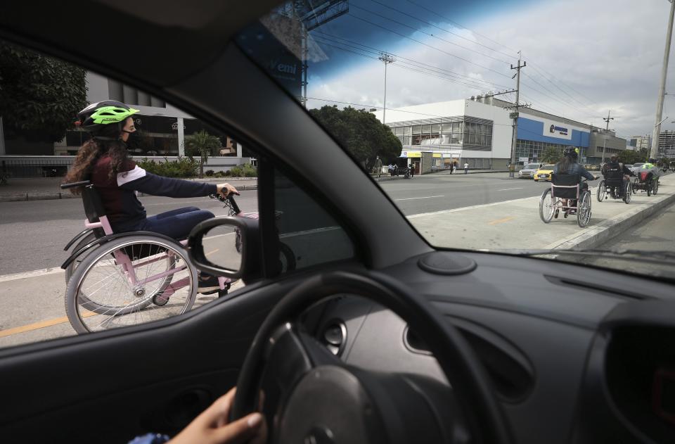 Tourists in electric wheelchairs ride in the streets of Medellin, Colombia, Wednesday, Nov. 18, 2020. To move tourists around the city, MATT uses electric hand-cycles that are powered by rechargeable batteries and latch on to wheelchairs with metal bars and hooks. (AP Photo/Fernando Vergara)