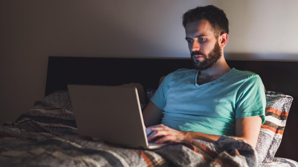 Young man working late in bed on a laptop.