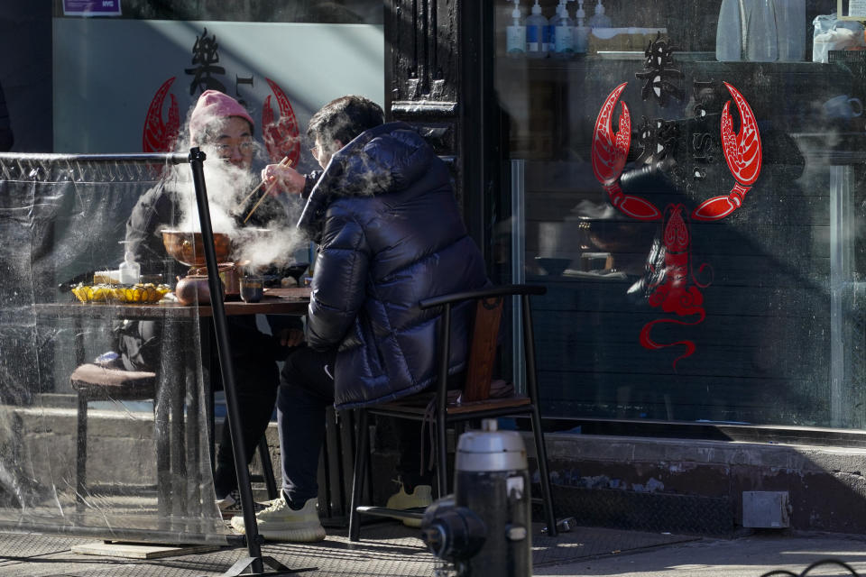 Steam rises from a dish as customers eat a meal on the sidewalk outside a restaurant, Sunday, Jan. 10, 2021, in the Hell's Kitchen neighborhood of New York. The boarded-up windows and For Rent signs are all over the place in Manhattan’s Hell’s Kitchen neighborhood. Nearby, the Broadway theaters are all dark. But the economic darkness brought on by the coronavirus pandemic has had a few bright spots. A couple of well-loved venues have gotten financial boosts, thanks to online fundraising campaigns and even a telethon. (AP Photo/Mary Altaffer)