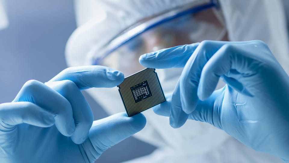 A worker in a white safety clothing holds up a semiconductor chip.