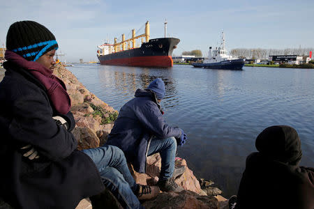 FILE PHOTO: Sudanese migrants sit on the bank, as a cargo makes its way along the Caen channel to the sea in Ouistreham, France, October 31, 2017. REUTERS/Pascal Rossignol/File Photo