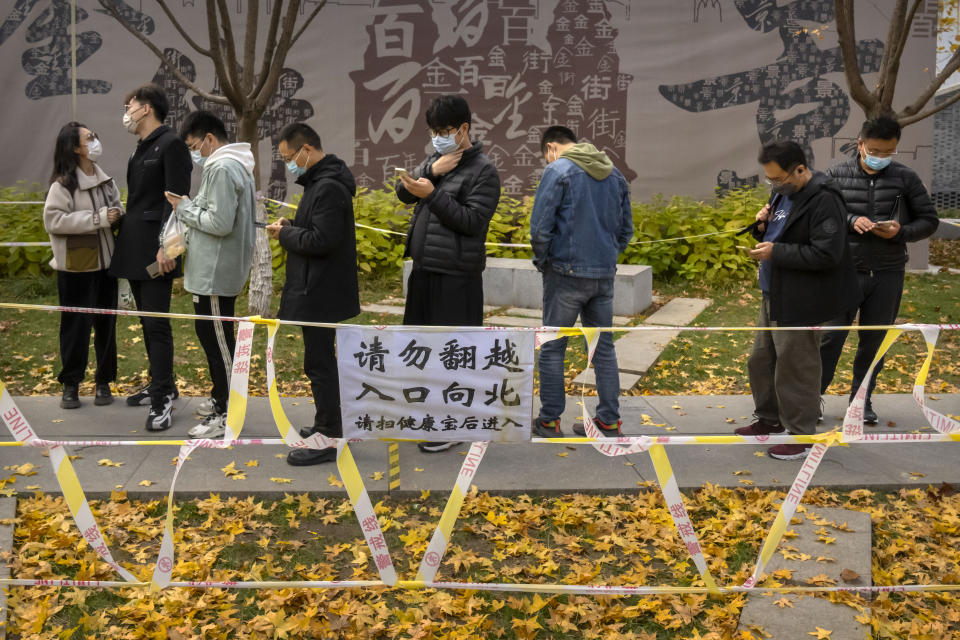 People wearing face masks stand in line for COVID-19 tests at a coronavirus testing site in Beijing, Saturday, Nov. 19, 2022. Performances have been suspended at one of Beijing's oldest and most renowned theaters amid a new wave of shop and restaurant closures in response to a spike in COVID-19 cases in the Chinese capital. (AP Photo/Mark Schiefelbein)