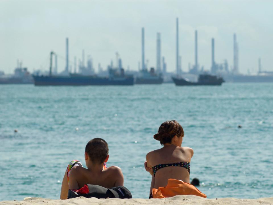 A couple sits on a beach in Sentosa before a view of an oil refinery in 2007.