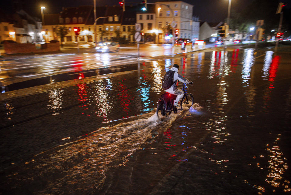 20 October 2023, Mecklenburg-Western Pomerania, Wismar: A cyclist rides through the high water at the city harbor in Wismar, Germany Friday, Oct. 20, 2023. Much of northern Europe braced for stormy weather, heavy rain and gale-force winds from the east. (Jens Büttner/dpa via AP)