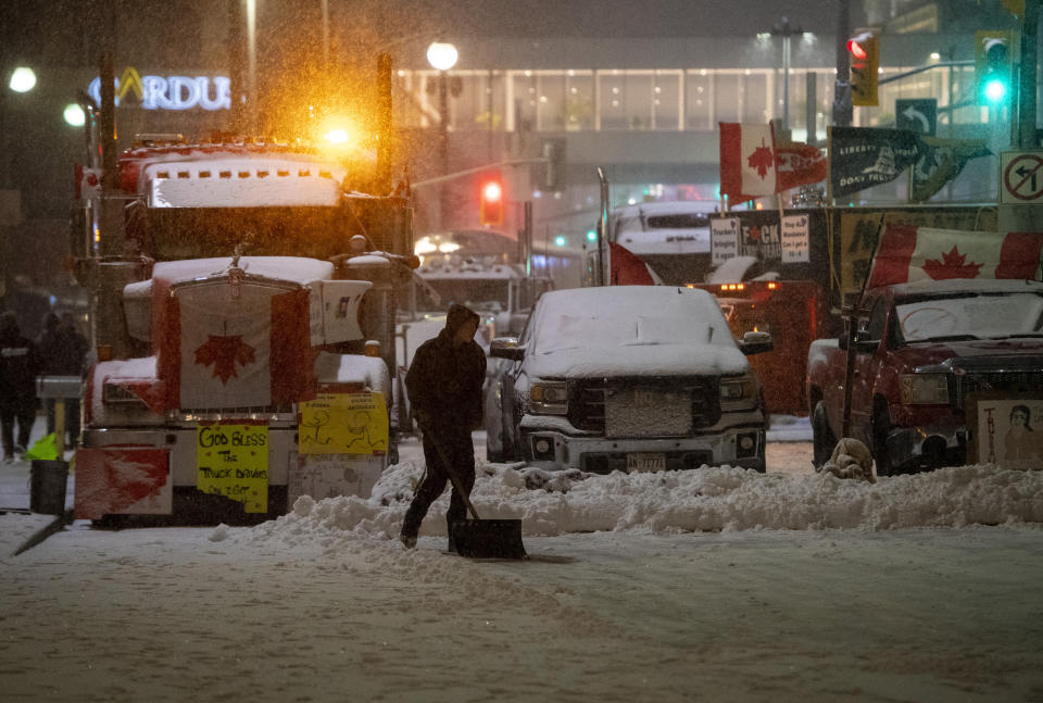 A protester shovels snow in front of parked semi-trailer and pickup trucks on Rideau Street, on the 21st day of a protest against COVID-19 measures that has grown into a broader anti-government protest, on Thursday, Feb. 17, 2022, in Ottawa. (Justin Tang/The Canadian Press via AP)