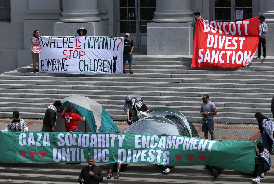 Protesters with banners advocating for Gaza, in a public demonstration on steps, some under makeshift tents