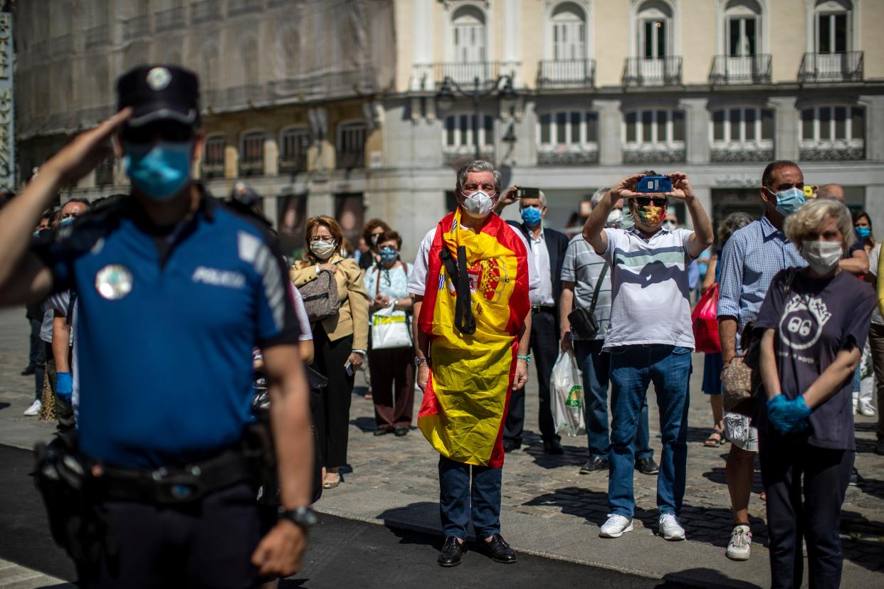 People hold a minute of silence for the victims of COVID-19 at Sol square in downtown Madrid, Spain, Wednesday, May 27, 2020. Flags are flying at half-mast on more than 14,000 public buildings in Spain as the European nation holds its first of 10 days of national mourning for the victims of the coronavirus.