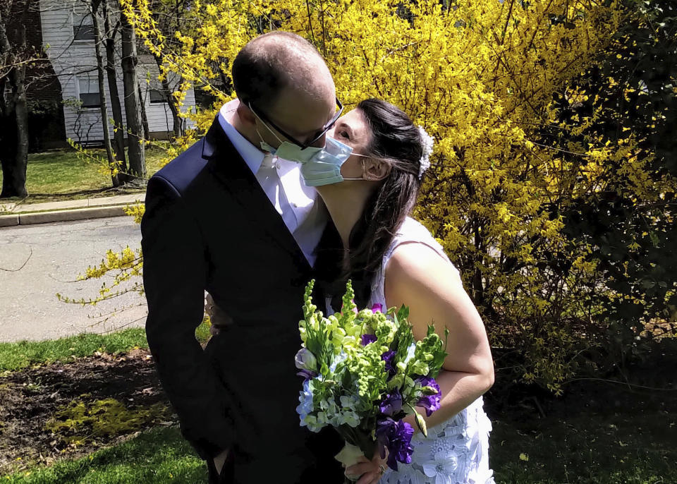 In this April 11, 2020, photo provided by Michael Wargo, newlyweds Danielle Cartaxo and Ryan Cignarella kiss while wearing masks after getting married in West Orange, N.J. Barred from getting married in a public space due to lockdown restrictions, Cartaxo and Cignarella got married on the front lawn of the home of a stranger who offered to help. (Michael Wargo via AP)
