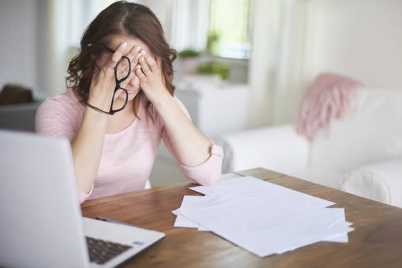 Woman sitting by a laptop and pile of papers covering her eyes