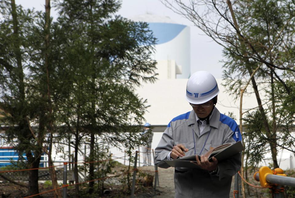 An employee of Kyushu Electric Power Co reads his memo in front of a reactor building at the company's Sendai nuclear power plant in Satsumasendai, Kagoshima prefecture April 3, 2014. While their reactors have been idled, Japan's nuclear plant operators have had to spend around $87 billion to burn replacement fossil fuels. This, in part, explains the utilities' estimated combined losses of around $47 billion as of March, and the $60 billion wiped off the companies' market value. Last week, Kyushu Electric Power Co was confirmed to be seeking a near $1 billion bailout in the form of equity financing from the government-affiliated Development Bank of Japan because of the cost of idling its reactors, joining Hokkaido Electric Power Co which has also asked the bank for financial backing. Picture taken April 3, 2014. REUTERS/Mari Saito (JAPAN - Tags: POLITICS ENERGY ENVIRONMENT)