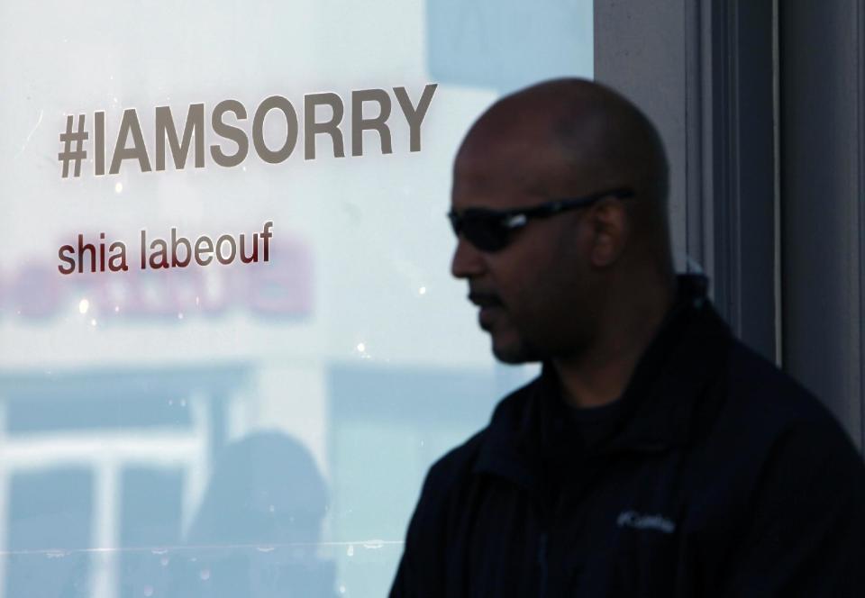 A security guard stands in front of the Stephen Cohen Gallery as visitors wait to enter for an exhibition, "#IAMSORRY" by actor Shia LaBeouf, in Los Angeles on Wednesday, Feb. 12, 2014. Seated at a small table, wearing a disheveled tuxedo and the paper bag with some eye holes cut out and the words "I AM NOT FAMOUS ANYMORE" scrawled in black ink across it, LaBeouf began his planned seven-hour, seven-day stint inside the small gallery on Tuesday, Feb. 11, 2014. (AP Photo/Richard Vogel)