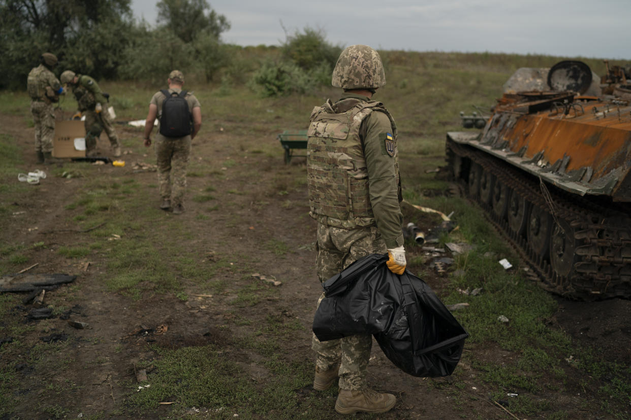 A Ukrainian serviceman carries a bag containing the remains of a body of a Russian soldier found inside at tank in a retaken area near the border with Russia in Kharkiv region, Ukraine, Saturday, Sept. 17, 2022. (AP Photo/Leo Correa)