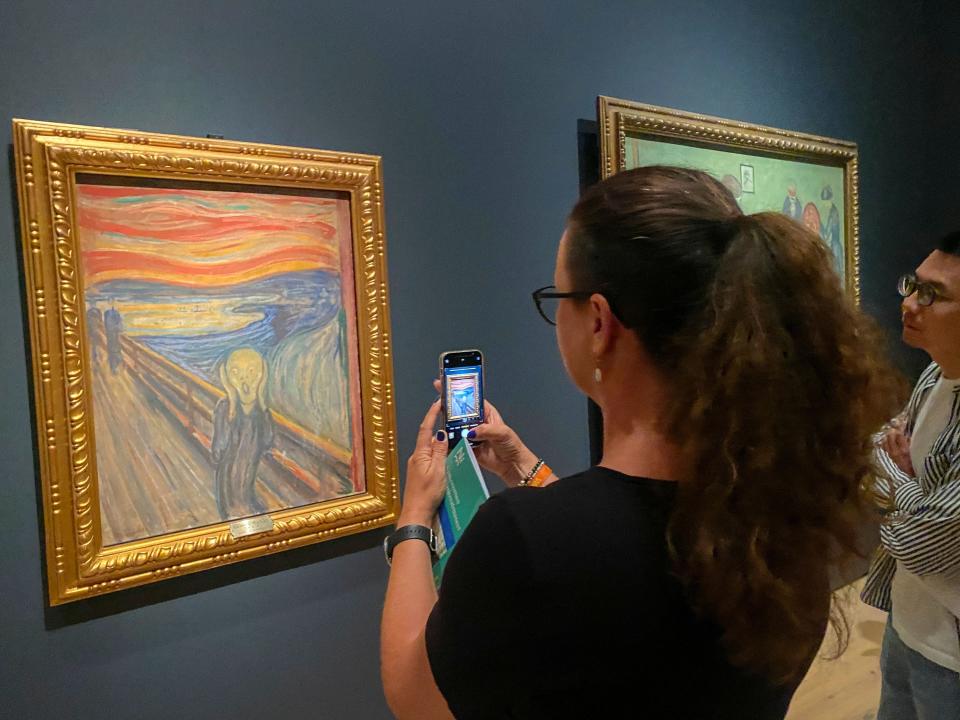 A visitor in a museum holds a phone up to take a picture of the painting "The Scream"