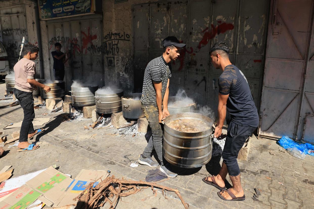 Two man carry a pot to be cooked on firewood as Gaza faces fuel and gas shortage (AFP via Getty Images)