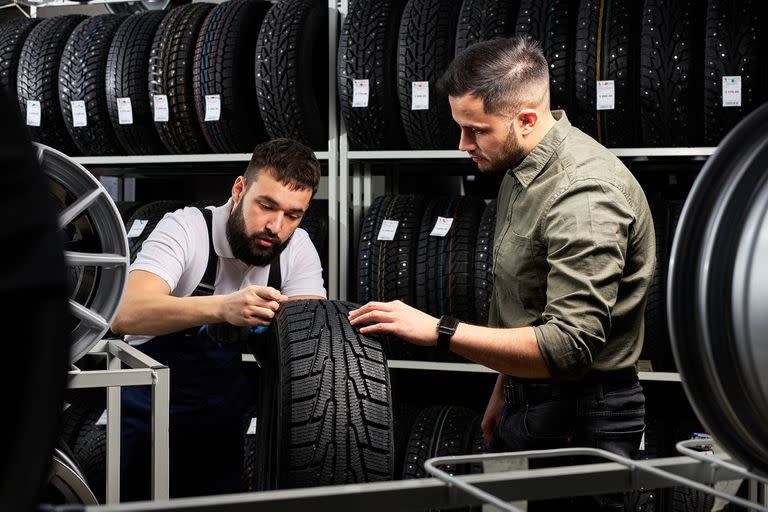 auto mechanic talk about advantages of auto tire to young client in service, man came to buy new tire for his automobile, stand talking and examining the product