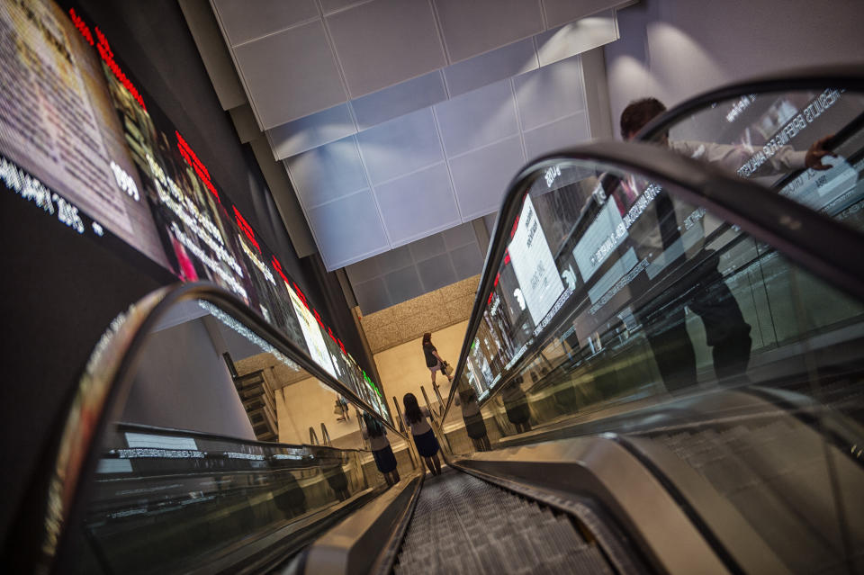 Pedestrians ride an escalator past an electronic screen and ticker board that indicates stock figures at the Singapore Exchange headquarters. (Photo: Getty Images)