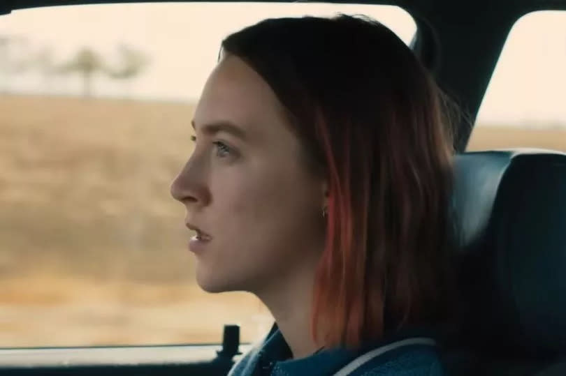 Saoirse Ronan with short, red hair in a bob sat in the driver's seat of a car