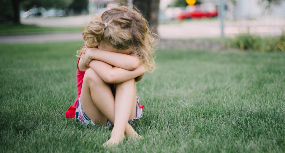 Pictured is a file picture of a young girl sitting on the grass with her face buried in her arms.