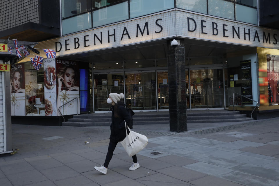 A woman wearing a face mask walks past the Debenhams flagship department store on Oxford Street, during England's second coronavirus lockdown in London, Tuesday, Dec. 1, 2020. In another dark day for the British retailing industry, Debenhams said Tuesday it will start liquidating its business after a potential buyer of the company pulled out, a move that looks like it will cost 12,000 workers their jobs. (AP Photo/Matt Dunham)