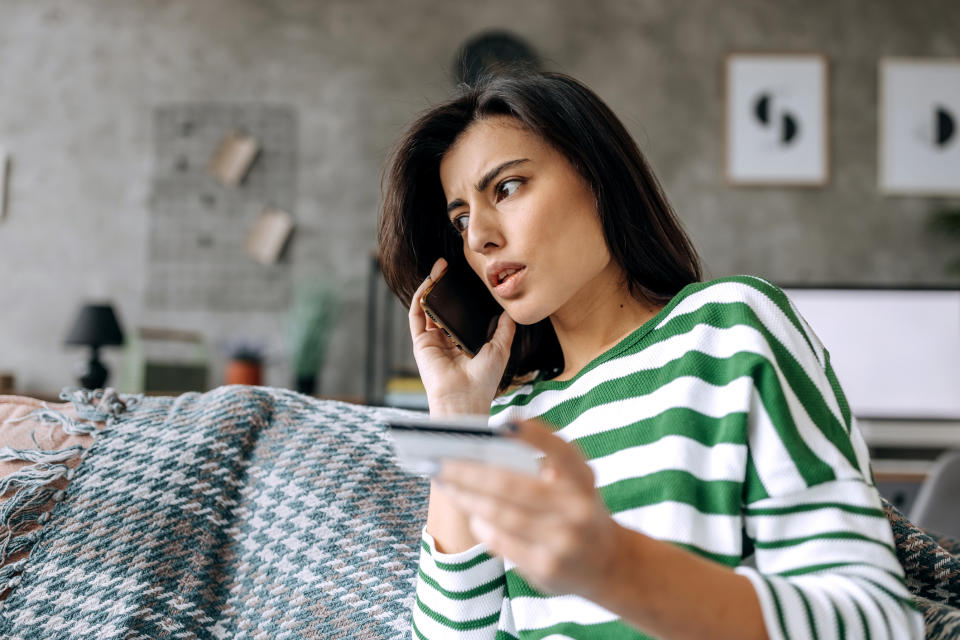 Woman in striped top looking puzzled while talking on phone and holding a card