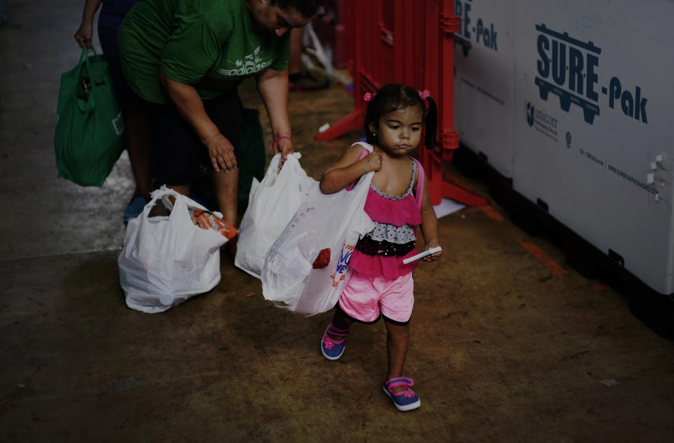 En esta fotografía del 13 de septiembre de 2018, una niña ayuda a su madre para cargar alimentos y otros productos de primera necesidad donados por la organización sin fines de lucro Ministerio MARC, en Manati, Puerto Rico. Los trabajadores de beneficencia dicen que el número de personas necesitadas que hacen cola para obtener alimentos se ha duplicado desde el huracán y que hay días en que se quedan sin alimentos. (AP Foto/Ramón Espinosa)