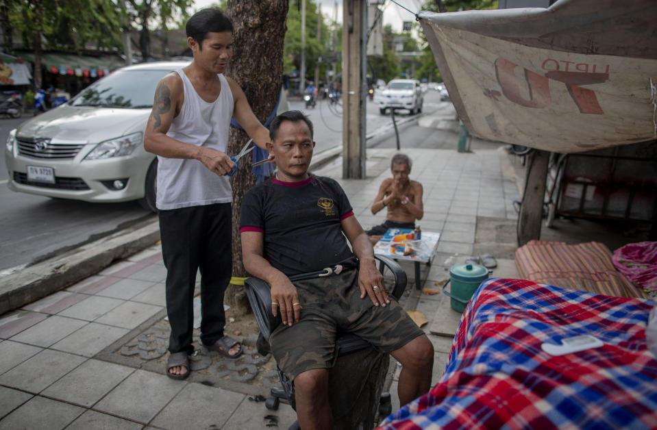 A man receives a haircut from a roadside barber in Bangkok, Thailand, Tuesday, June 23, 2020. Daily life in the capital is resuming to normal as the Thai government continues to ease restrictions related to running business and activities that were imposed weeks ago to combat the spread of COVID-19. (AP Photo/ Gemunu Amarasinghe)