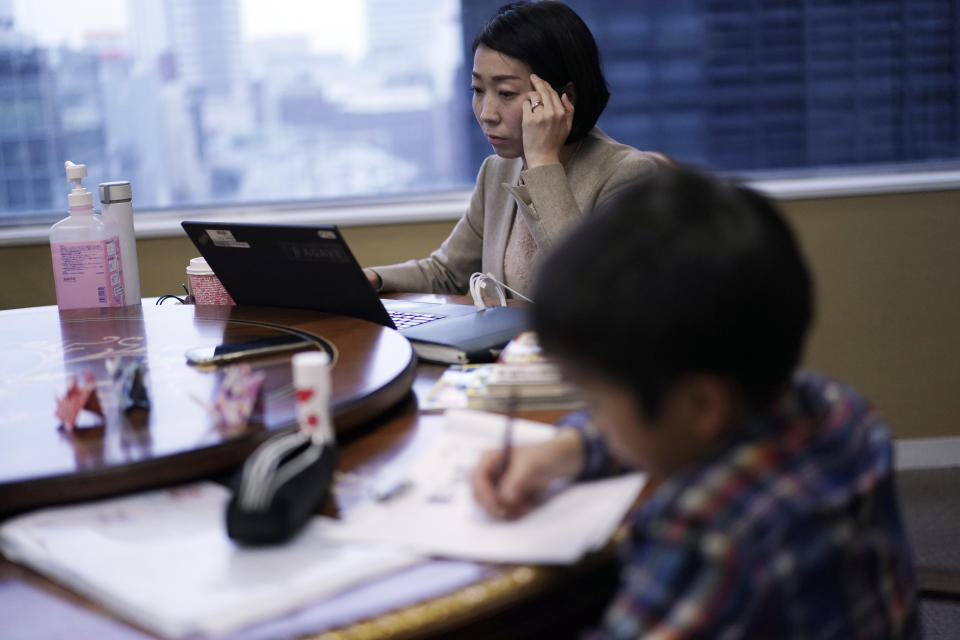Keiko Kobayashi, an employee at the staffing services company Pasona Inc., works as her son does his homework at the company's headquarters Monday, March 2, 2020, in Tokyo. Many Japanese schools were shut down Monday and spring holidays began unexpectedly early for children as part of a government-led measure to prevent further escalation of the coronavirus. (AP Photo/Eugene Hoshiko)