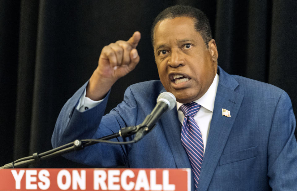 Republican conservative radio show host Larry Elder speaks into a microphone at a podium with a sign reading: Yes on recall