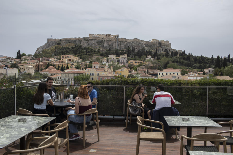 People sit in on a cafe terrace, in the Monastiraki district of Athens, with the ancient Acropolis hill in the background, Monday, May 3, 2021. Cafes and restaurants have reopened in Greece for sit-down service for the first time in nearly six months, as the country began easing coronavirus-related restrictions with a view to opening to the vital tourism industry in the summer. (AP Photo/Petros Giannakouris)