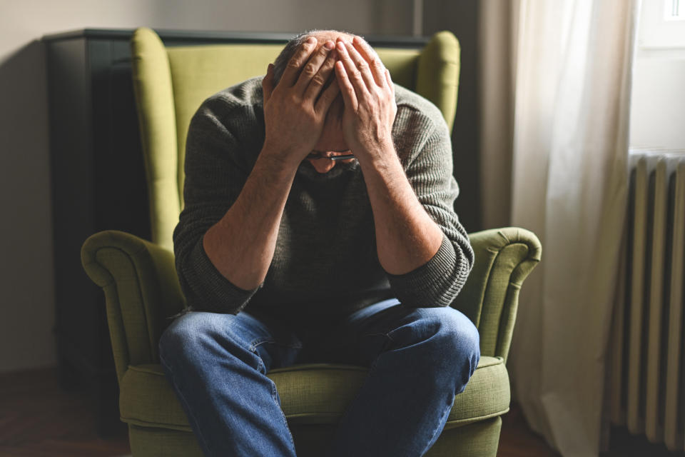 A man sits in an armchair with his head in his hands, appearing distressed or in deep thought