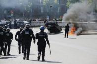 French riot police stand next to an overturned car as striking French taxi drivers demonstrate at the Porte Maillot to block the traffic on the Paris ring road during a national protest against car-sharing service Uber, in Paris, France, June 25, 2015. (REUTERS/Charles Platiau)