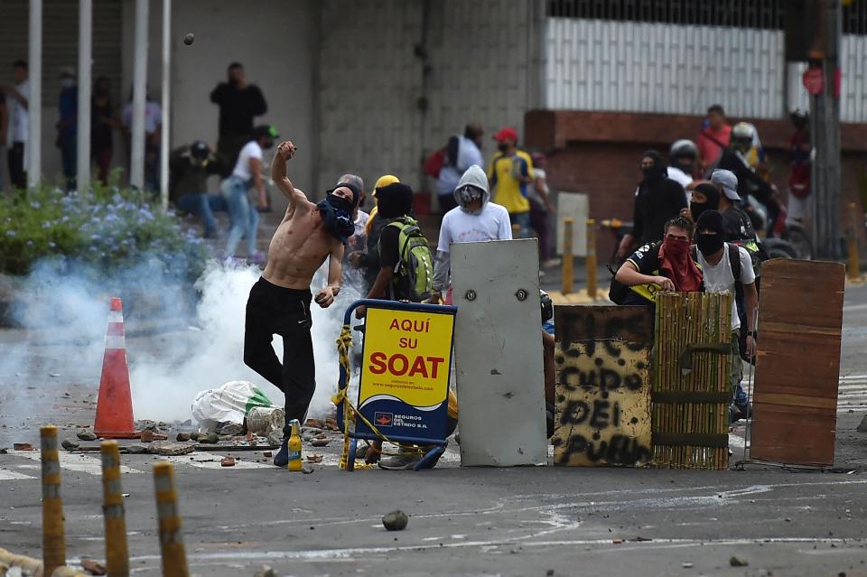 A demonstrator throws a rock to riot police officers during a protest against the government in Cali, Colombia, on May 10, 2021. - Faced with angry street protests and international criticism over his security forces' response, Colombia President Ivan Duque is coming across as erratic and out of touch with a country in crisis, analysts say. Since April 28, hundreds of thousands of people have vented their frustrations against the government after poverty and violence soared during the pandemic. (Photo by Luis ROBAYO / AFP) (Photo by LUIS ROBAYO/AFP via Getty Images)