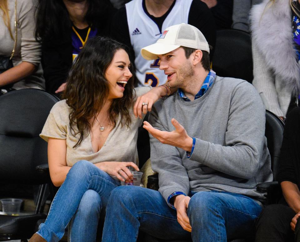 Mila Kunis sits with Ashton Kutcher at a game