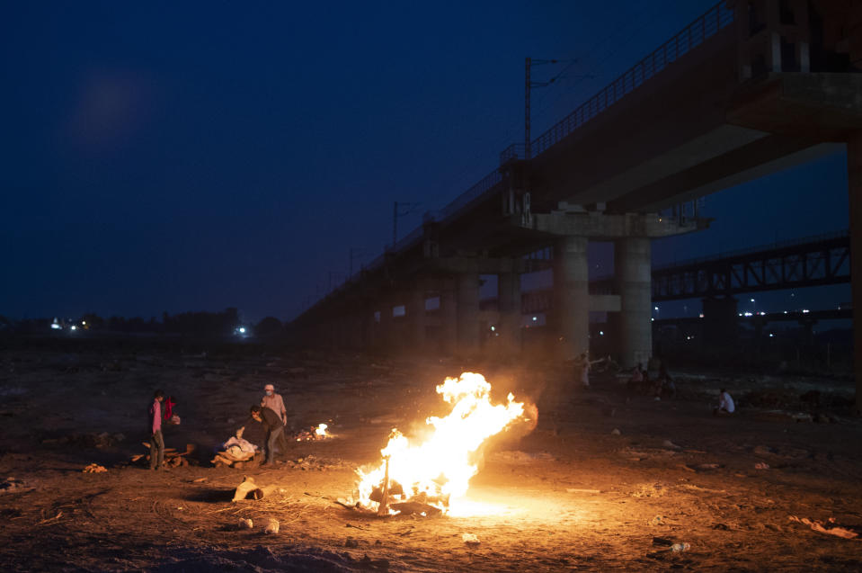 Relatives stand near the funeral pyre of their loved one who died due to COVID-19 at a cremation ground in Prayagraj, India, Saturday, May 8, 2021. (AP Photo/Rajesh Kumar Singh)